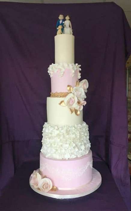 Extra large pink and ivory wedding cake with hand painted gold and added ruffles with large handmade sugar roses and a cake topper made of shore also and to add a find of touch some demask