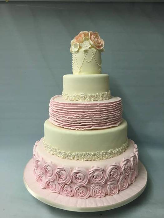 Extra large wedding cake in a sugar pink and ivory icing with hand piped ruffles and rosettes and hand piped pearls and  flowers on the top