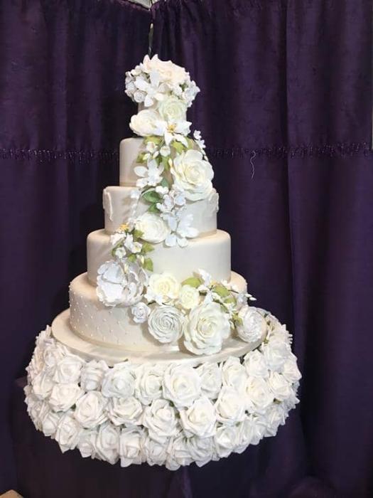 Extra large wedding cake with cascading extra large roses and greenery sitting on the bed of silk flower