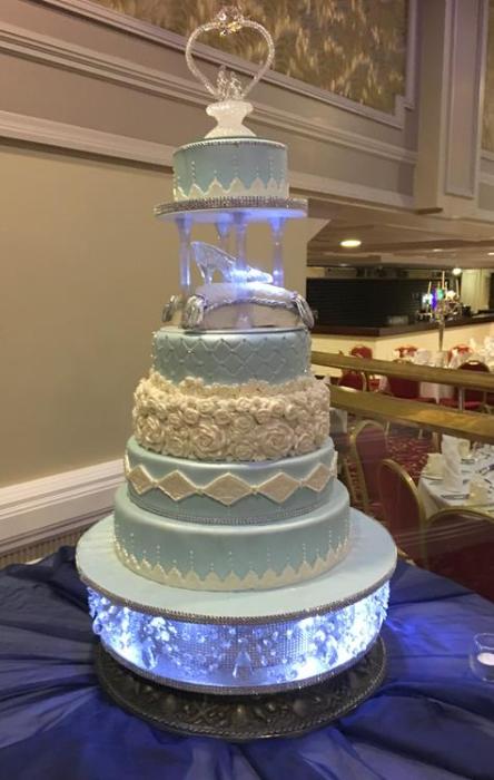 Extra large wedding cake in the pastel blue and white icing decorated with lace pieces and flowers Cinderella inspired the added cushion cake and glass slipper to top it all off