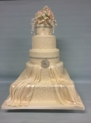 Extra large wedding cake in different shapes around square with a satin dry and Diamond  brooch topped off with  sugar flowers