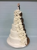 Extra large wedding cake split design half icing and half chocolate with a dripping effect but cascading  sugar roses  to separate both sides with ceramic bride and groom