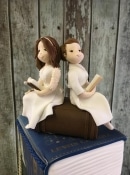2 brides sitting on a book  sugar wedding cake toppers
