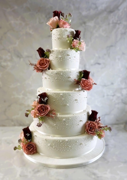 Iced large wedding cake with edible pearls and hand painted with silk flowers