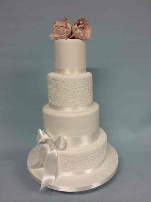 Delicate hand piped White wedding cake with white satin bow and Pink flowers